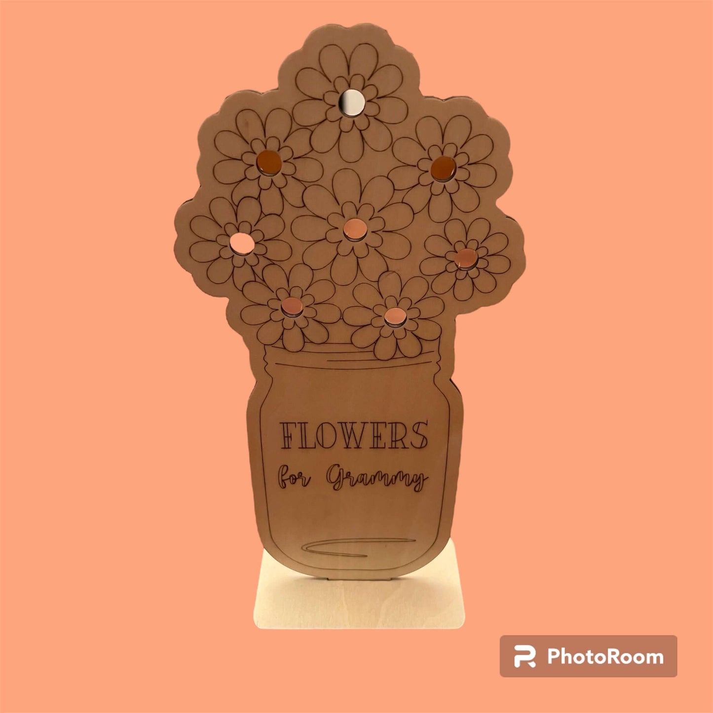 The Flower Holder for a Special Person by Wet Nose Woodworks, shaped like a flower bouquet in a jar with “FLOWERS for Grandma” engraved, stands on a table against a softly blurred window backdrop.