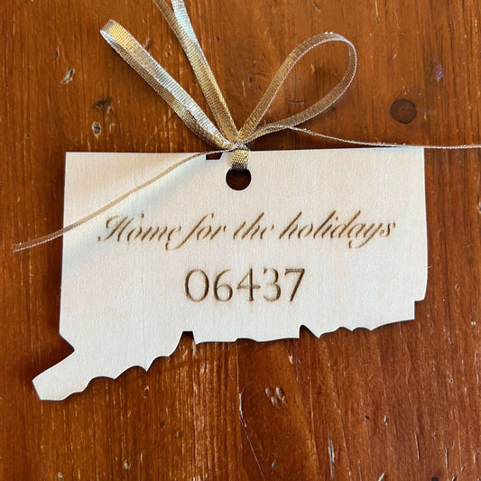 The Connecticut State Ornament with Personalization by Wet Nose Woodworks is a handcrafted wooden keepsake engraved with Home for the holidays and zip code 06437, tied with a gold ribbon to showcase Connecticut pride.