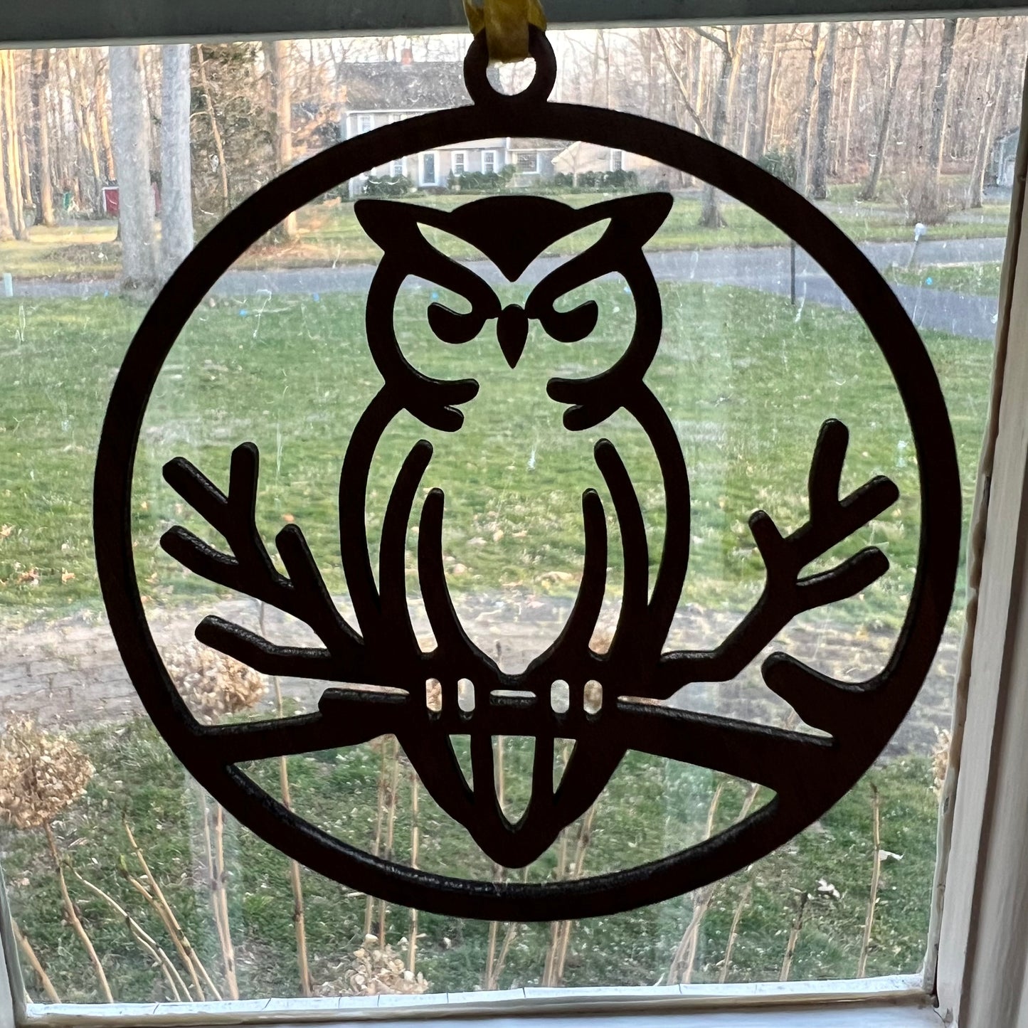 The Owl ornament by Wet Nose Woodworks is a decorative metal silhouette of an owl on a branch, perfect for hanging in your window as an eco-friendly rustic home accent.