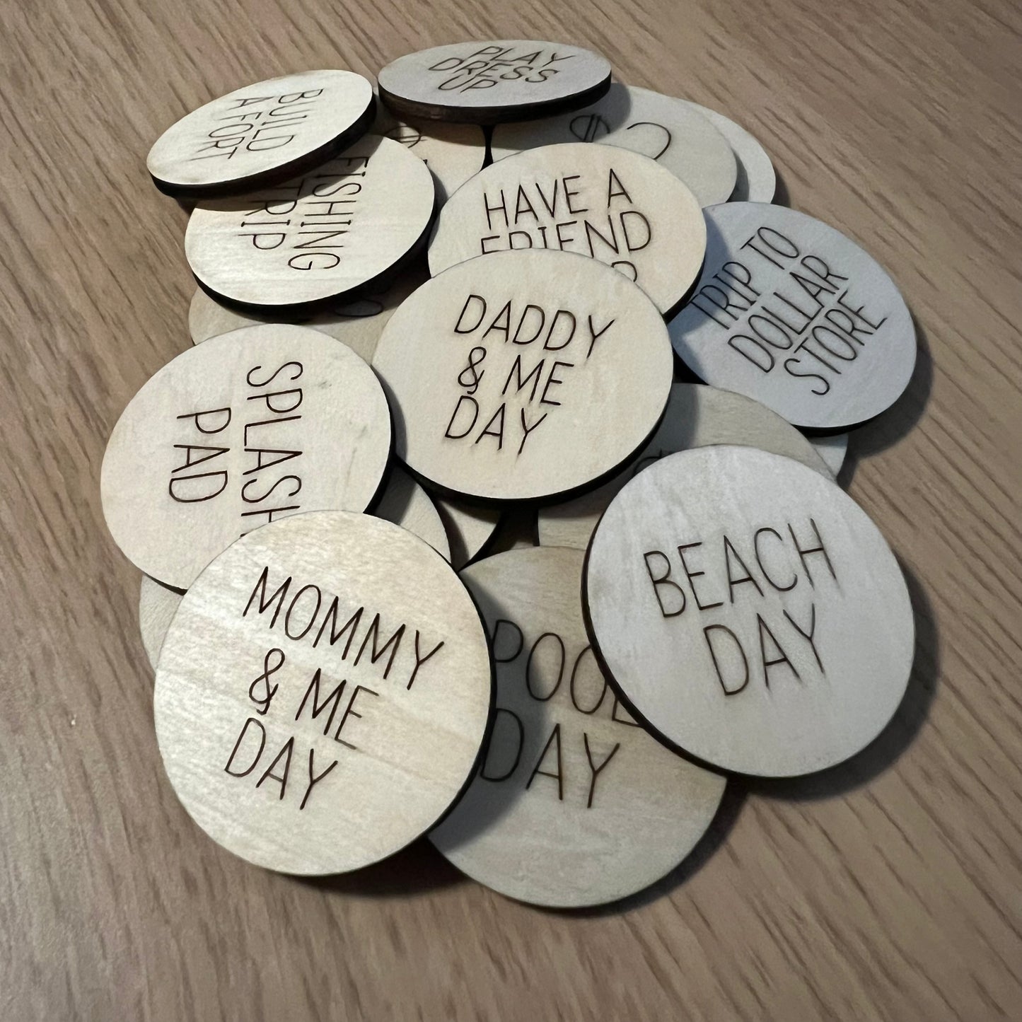Wet Nose Woodworks Reward Tokens—laser engraved wood tokens with phrases like MOMMY & ME DAY, DADDY & ME DAY, and BEACH DAY—are scattered on a light wood surface.
