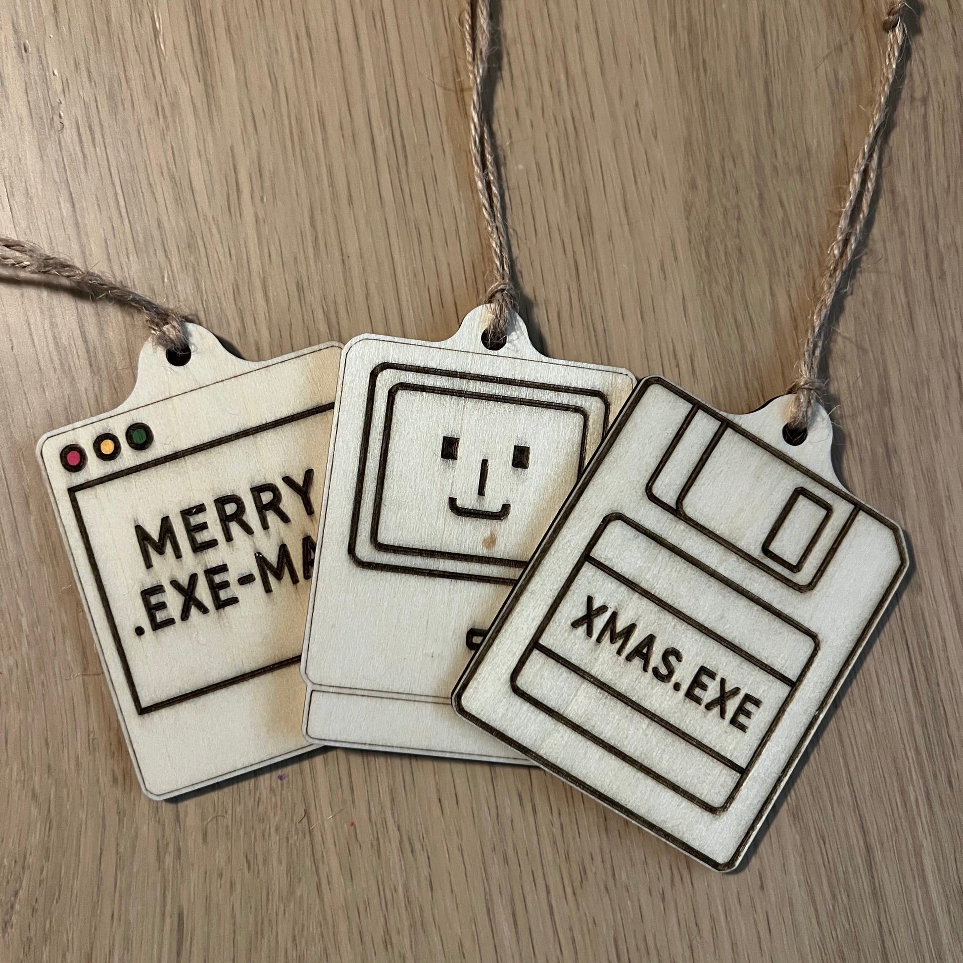 Three floppy disc-shaped Christmas tags with text and a smiley face on a wooden surface.