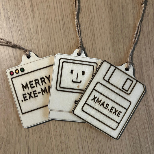 Three floppy disc-shaped Christmas tags with text and a smiley face on a wooden surface.