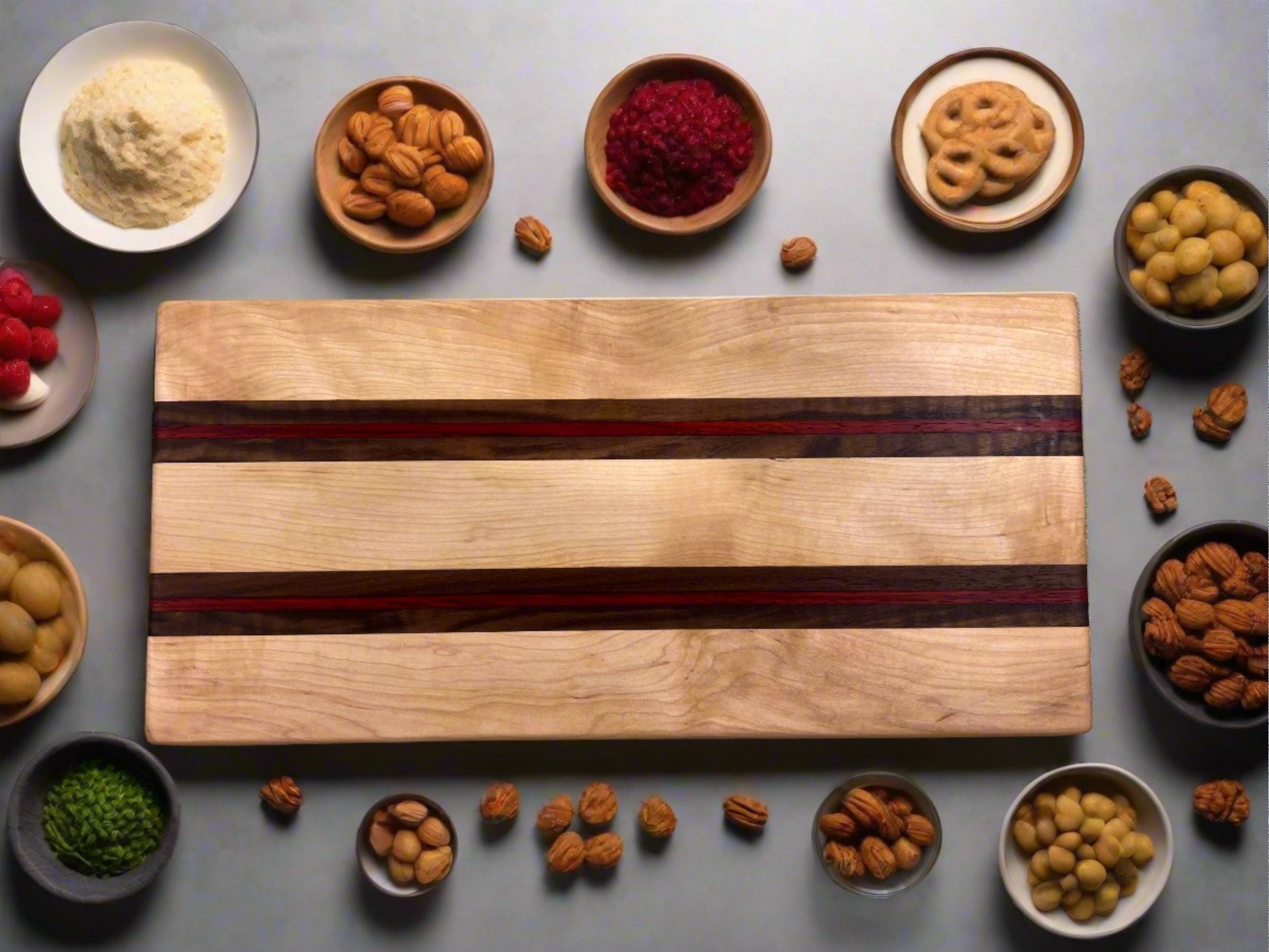 The Artisan Board #1 by Wet Nose Woodworks, featuring a dark inlay, sits centered on a table surrounded by bowls of snacks. The board is empty and ready for your next food prep or serving event.