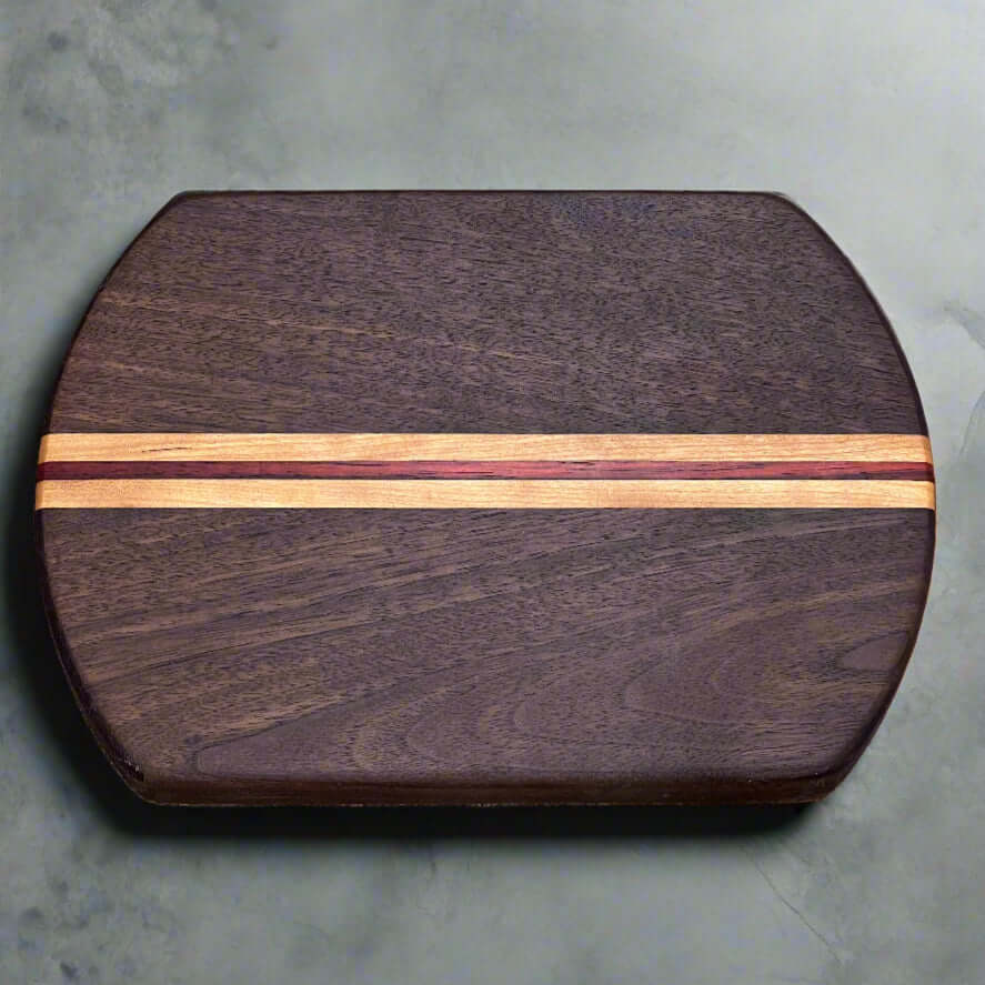 The Artisan Board #12 by Wet Nose Woodworks is an oval, dark wooden charcuterie board featuring two narrow, light stripes running lengthwise down the center, highlighting expert craftsmanship. Shown here on a gray surface.