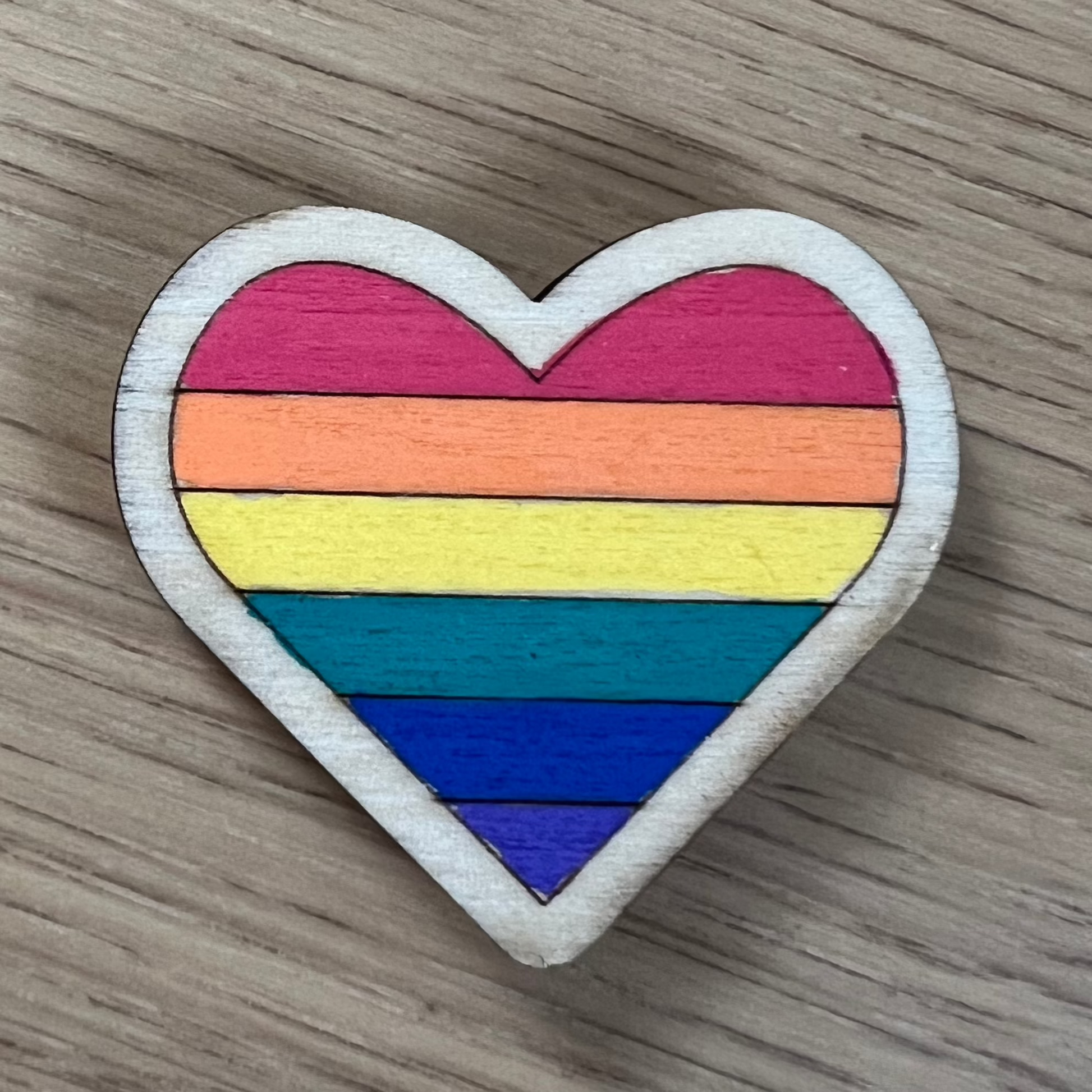 Hand-painted wooden magnet featuring a colorful rainbow Pride flag design on a heart shaped wooden base.