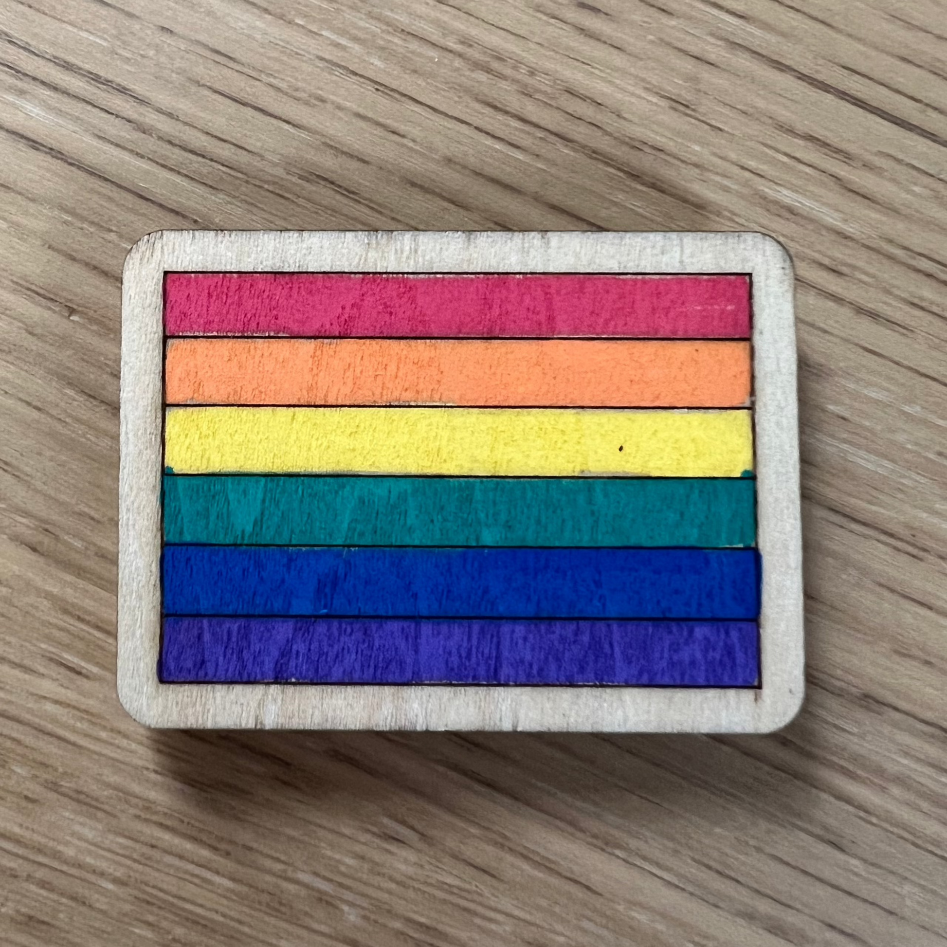 Hand-painted wooden magnet featuring a colorful rainbow Pride flag design on a wooden base.