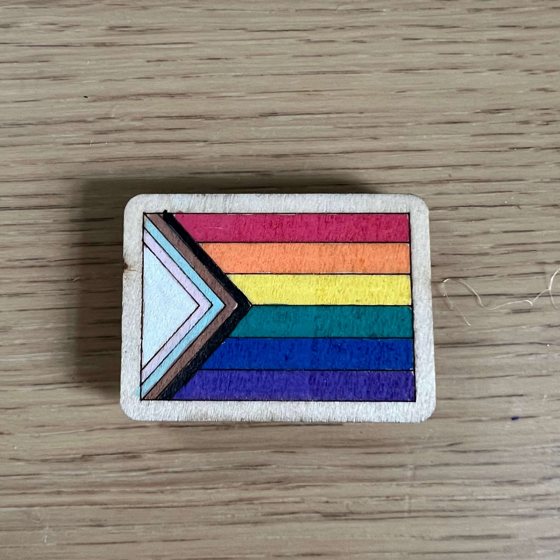 Hand-painted wooden magnet featuring a colorful rainbow Pride flag design on a wooden base.