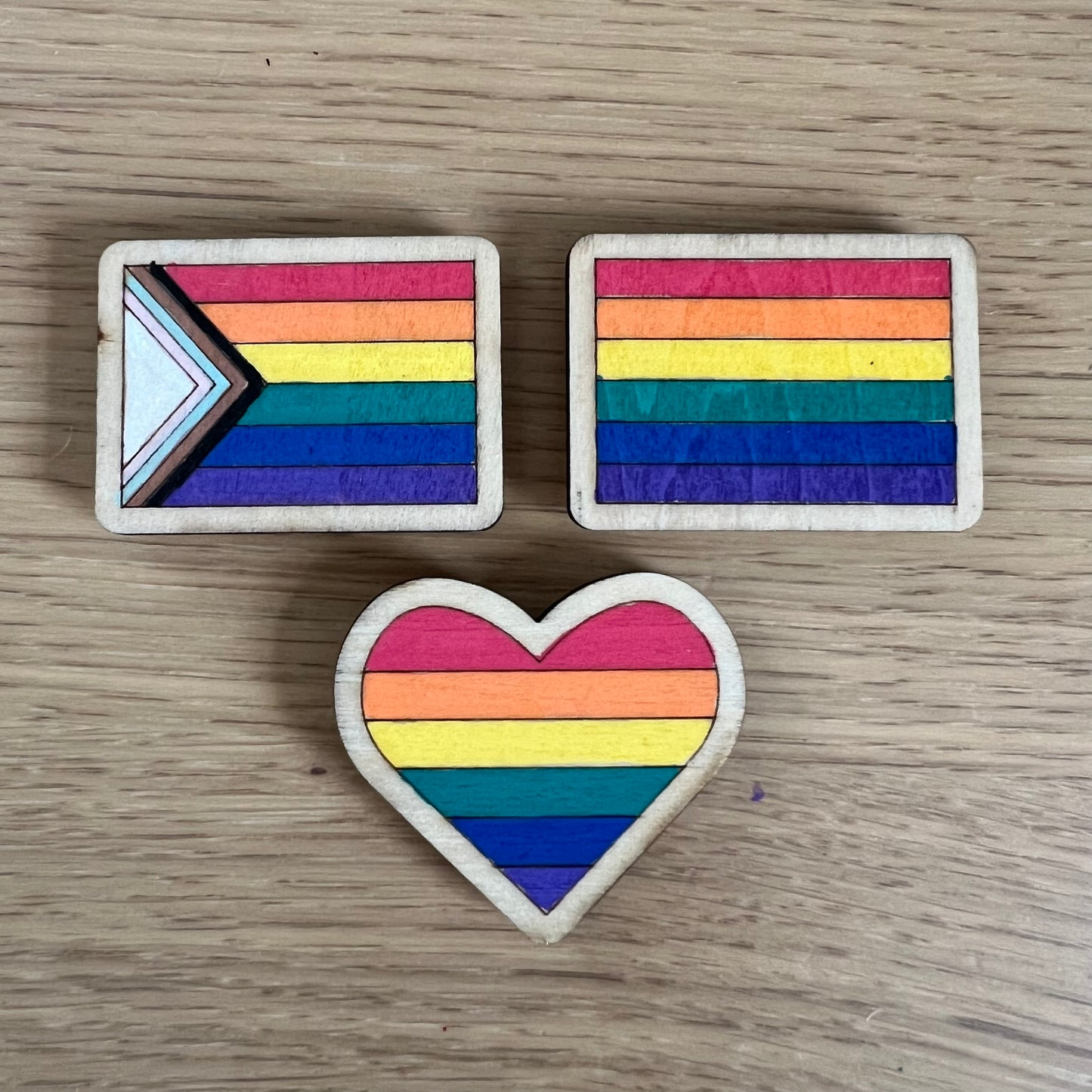 Hand-painted wooden magnet featuring a colorful rainbow Pride flag design on a wooden base.