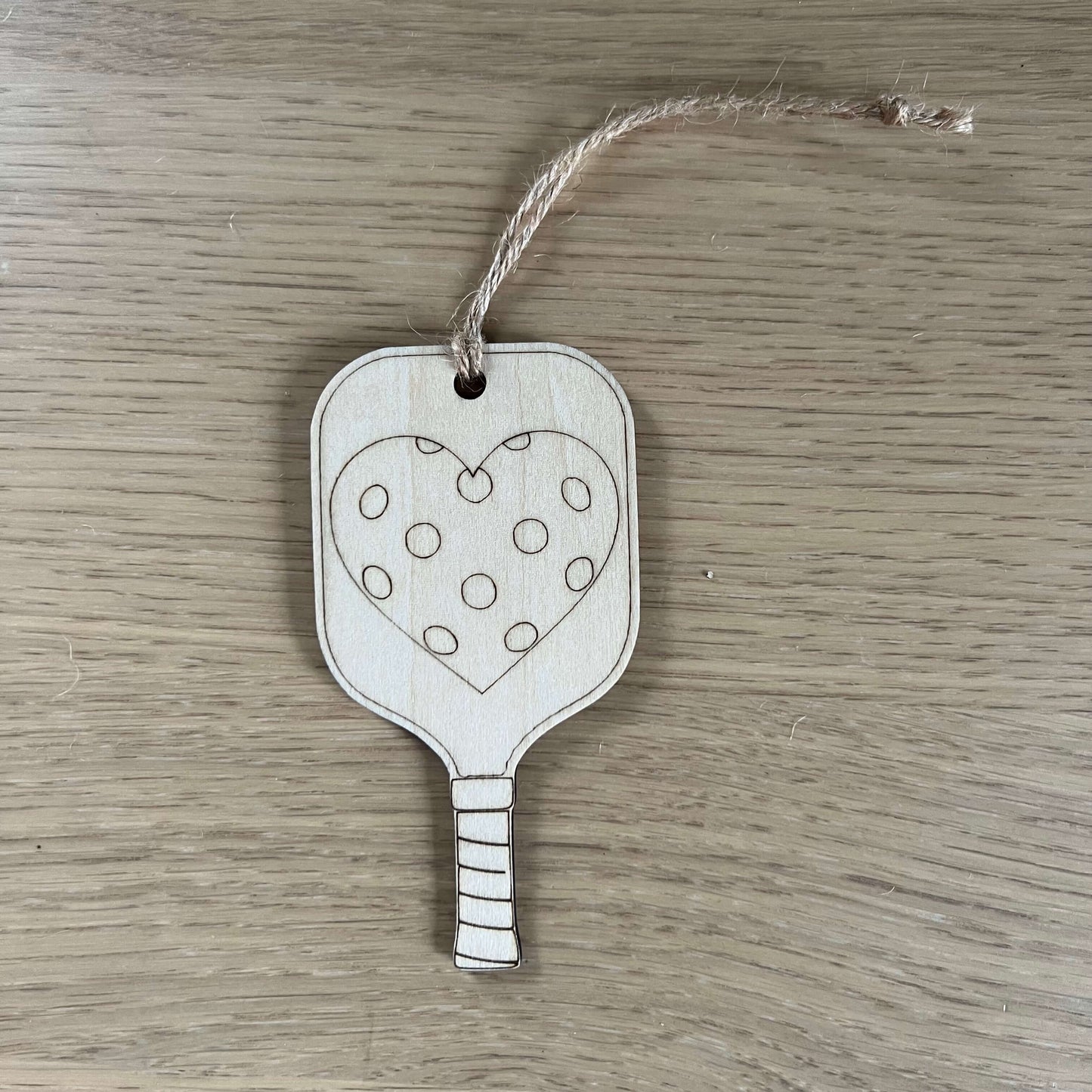 The I Heart Pickleball Ornament by Wet Nose Woodworks features two wooden pickleball paddle tags with strings—one saying I ♥ Pickleball and the other with a polka dot heart. A unique, charming gift for any pickleball enthusiast.