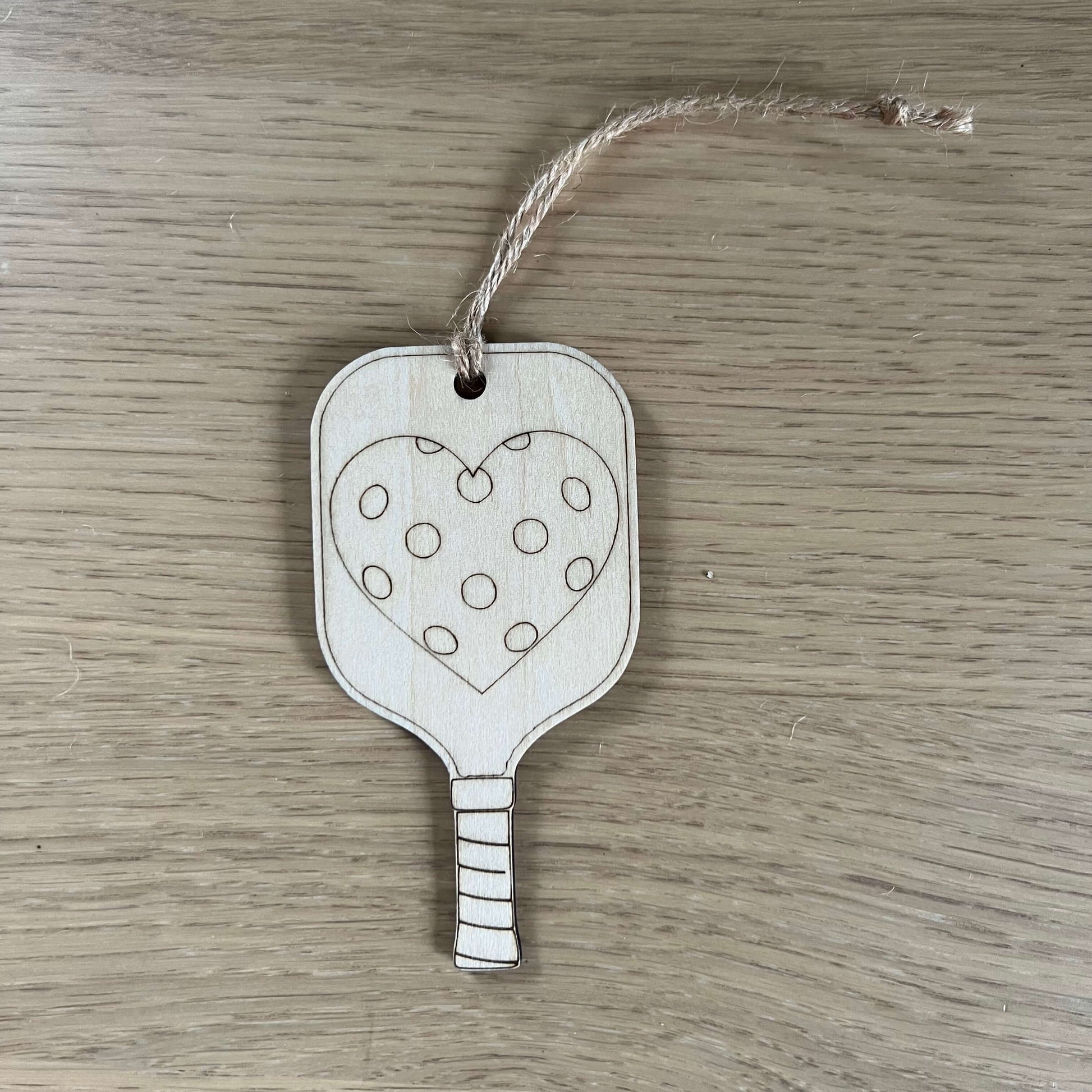 The I Heart Pickleball Ornament by Wet Nose Woodworks features two wooden pickleball paddle tags with strings—one saying I ♥ Pickleball and the other with a polka dot heart. A unique, charming gift for any pickleball enthusiast.