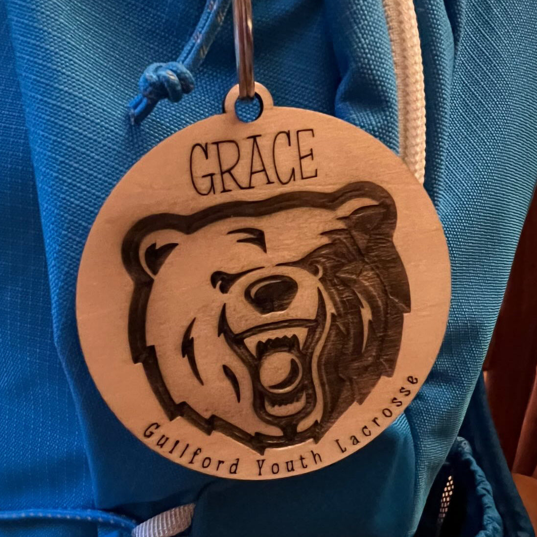 Wooden tag with bear design and 'Grace' text attached to a blue bag.