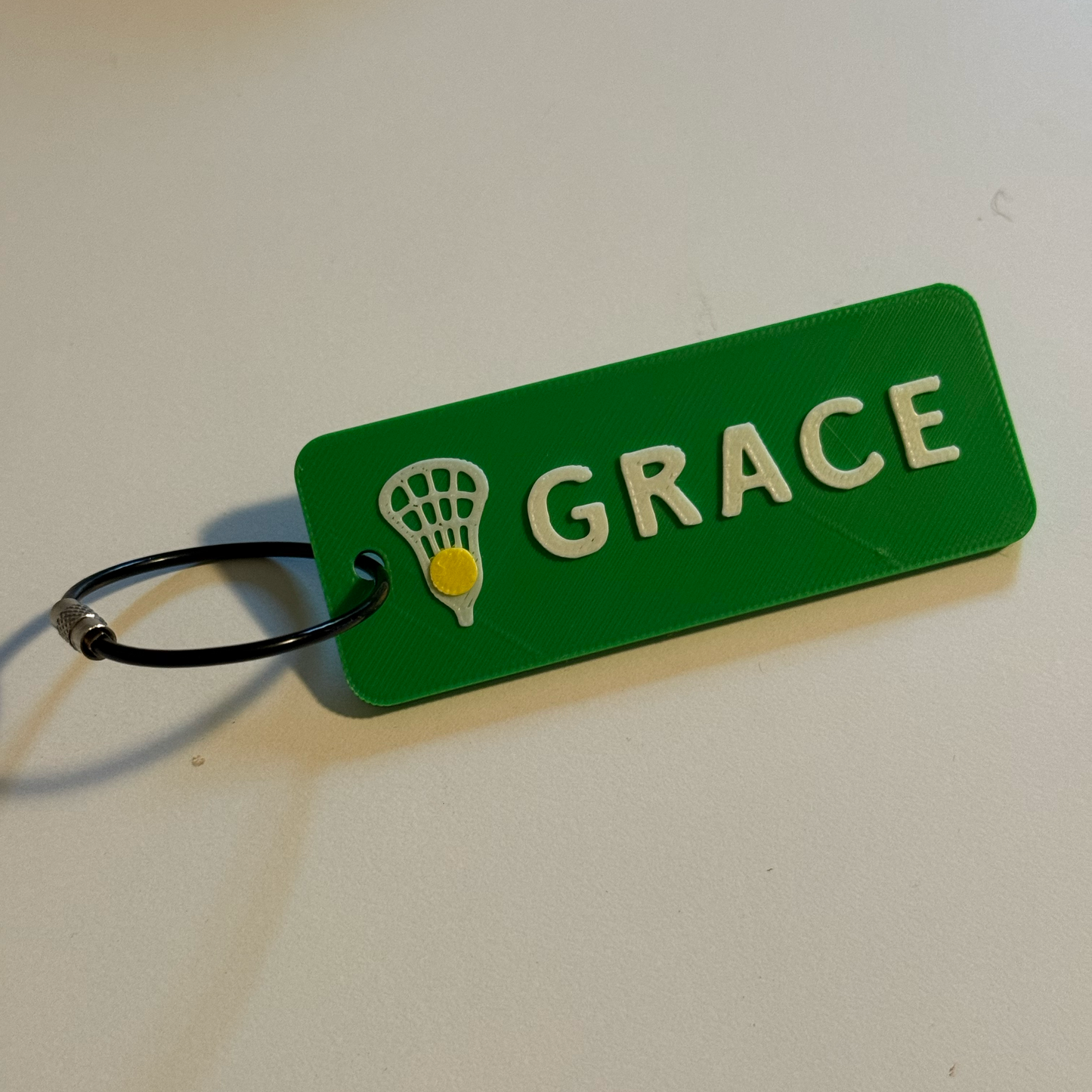 Green tag with 'GRACE' and a lacrosse ball symbol on a white background