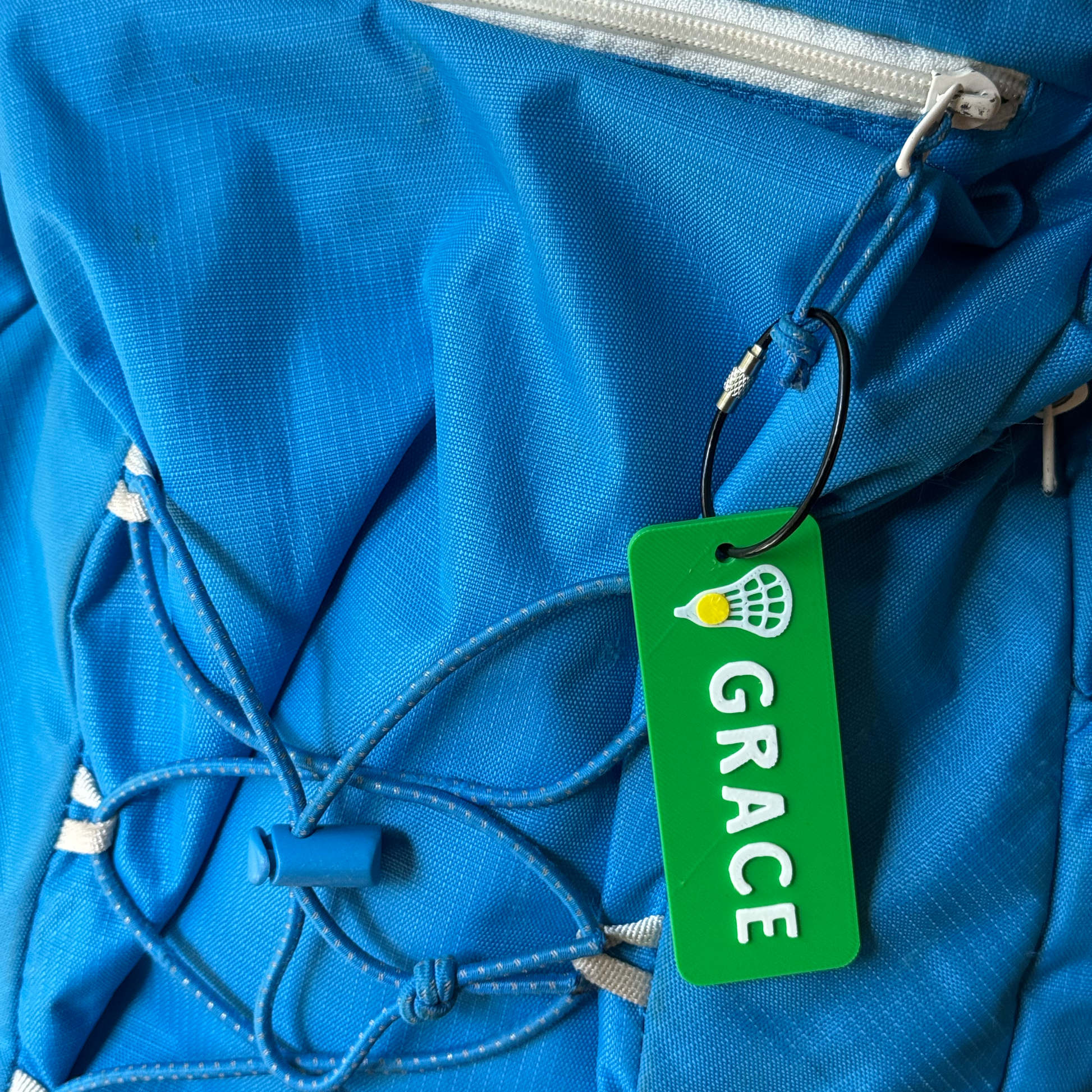 Custom lacrosse name tag clipped to a blue sports bag strap