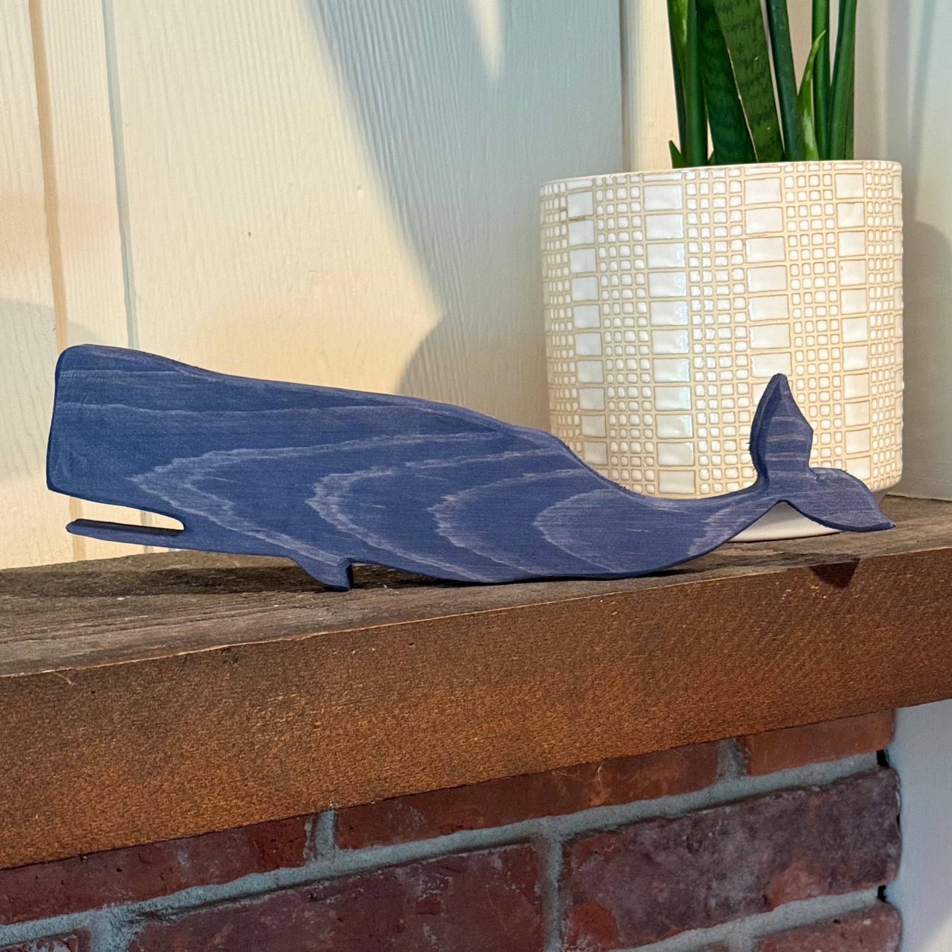 Blue whale-shaped figurine on a wooden mantle next to a brick wall