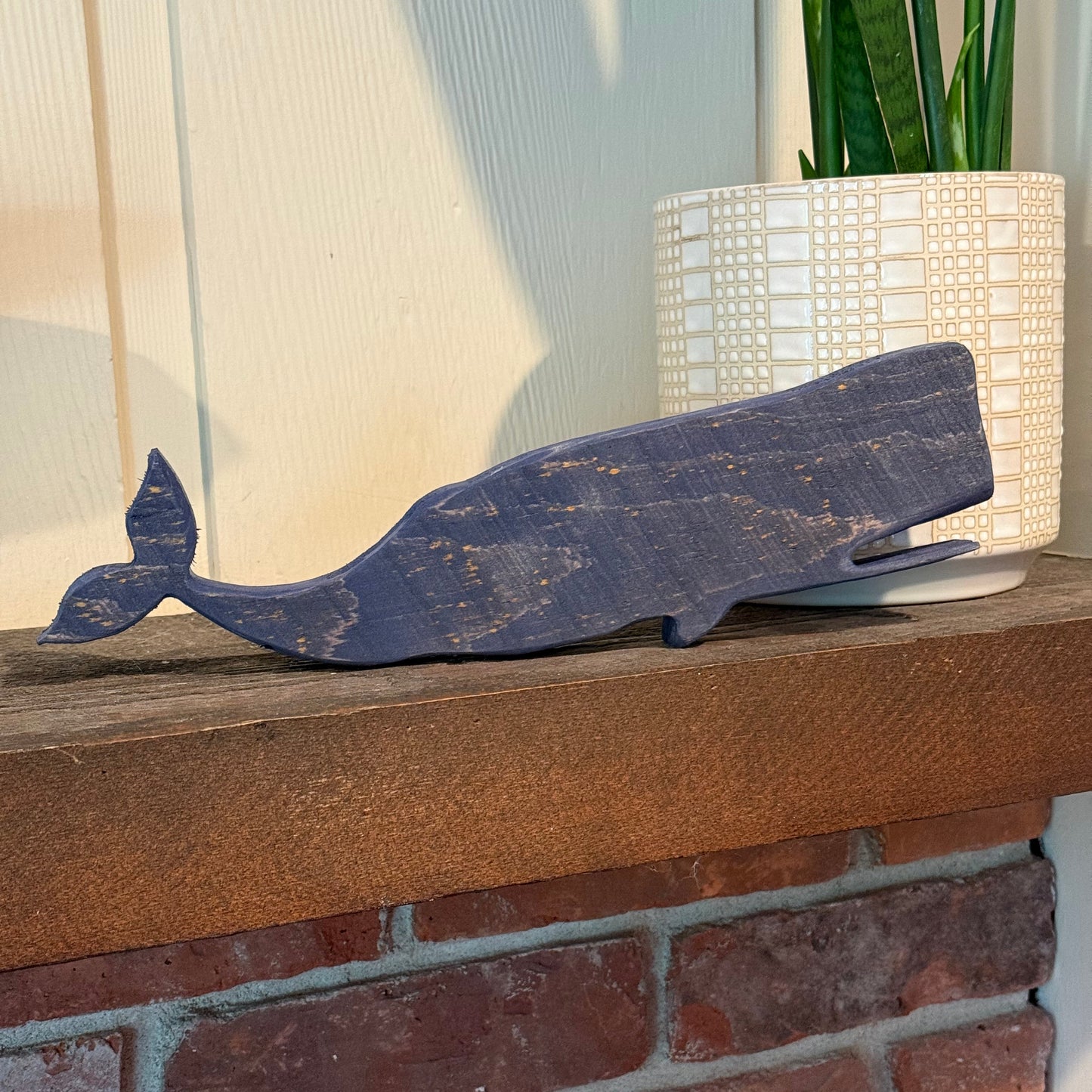 Wooden whale decoration leaning against a brick wall.