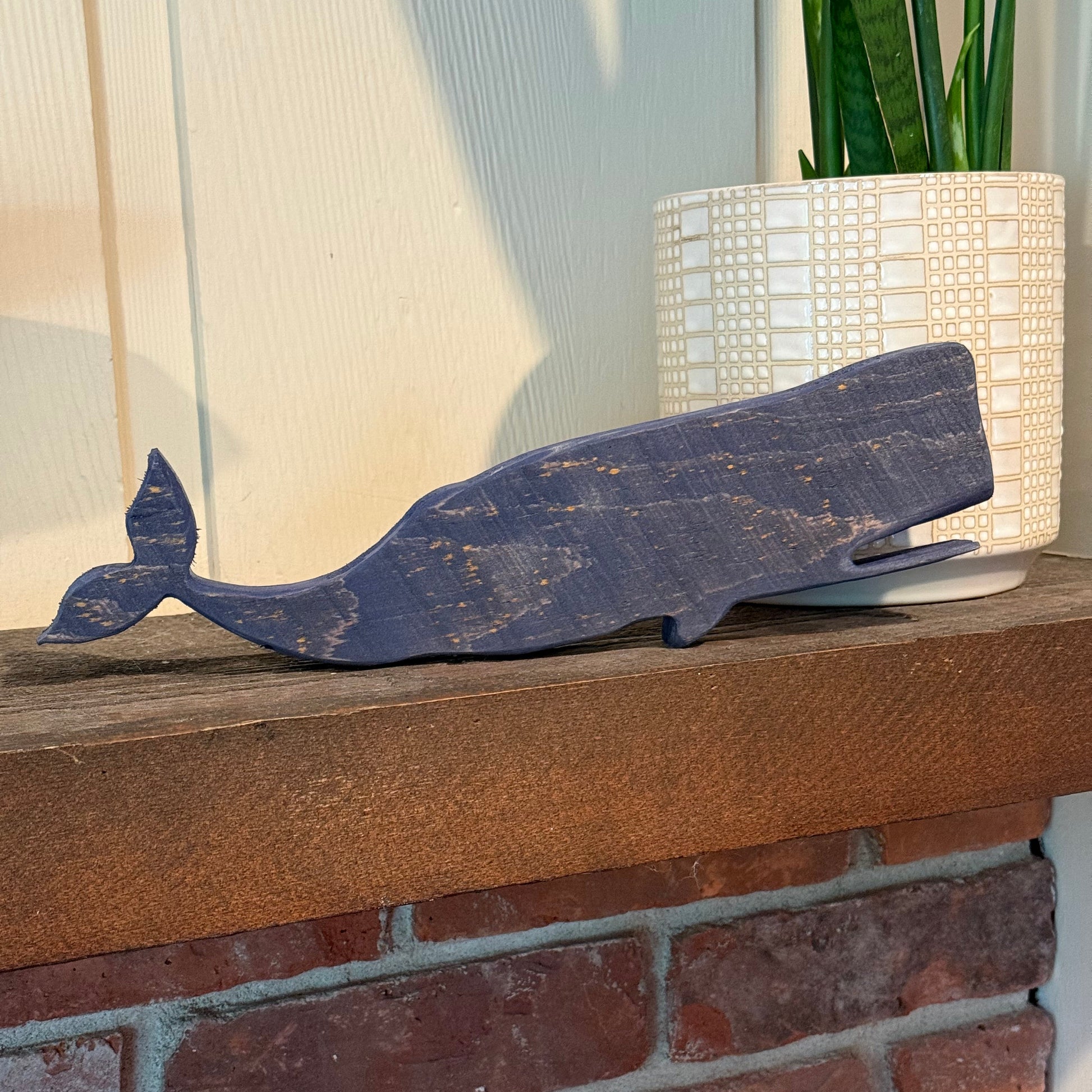 Wooden whale decoration leaning against a brick wall.
