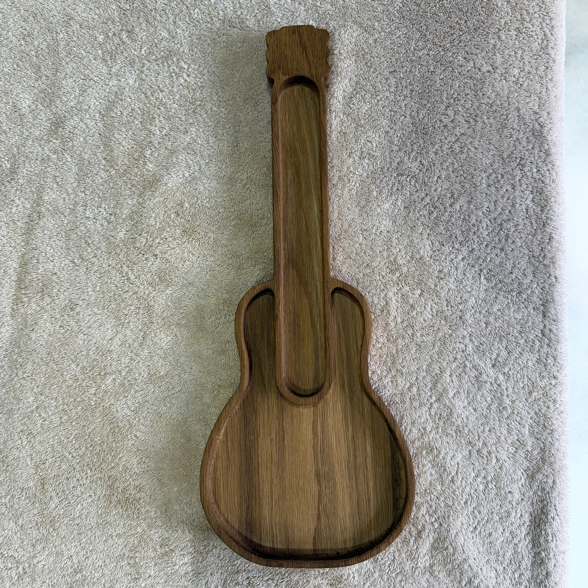 A small wooden guitar-shaped tray or dish with a natural wood grain finish, placed on a textured off-white towel background.