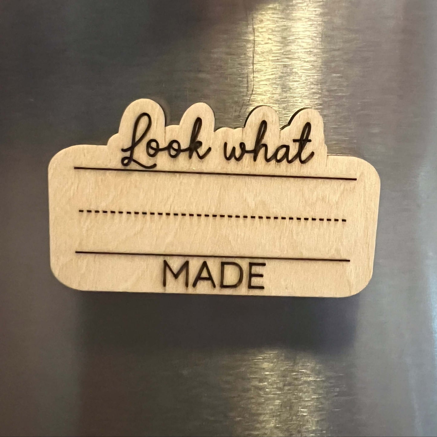 The Wet Nose Woodworks Look What I Made Fridge Magnet lets you proudly display and personalize your childs art or schoolwork with their name in colorful marker, adding a natural wood touch to your fridge.