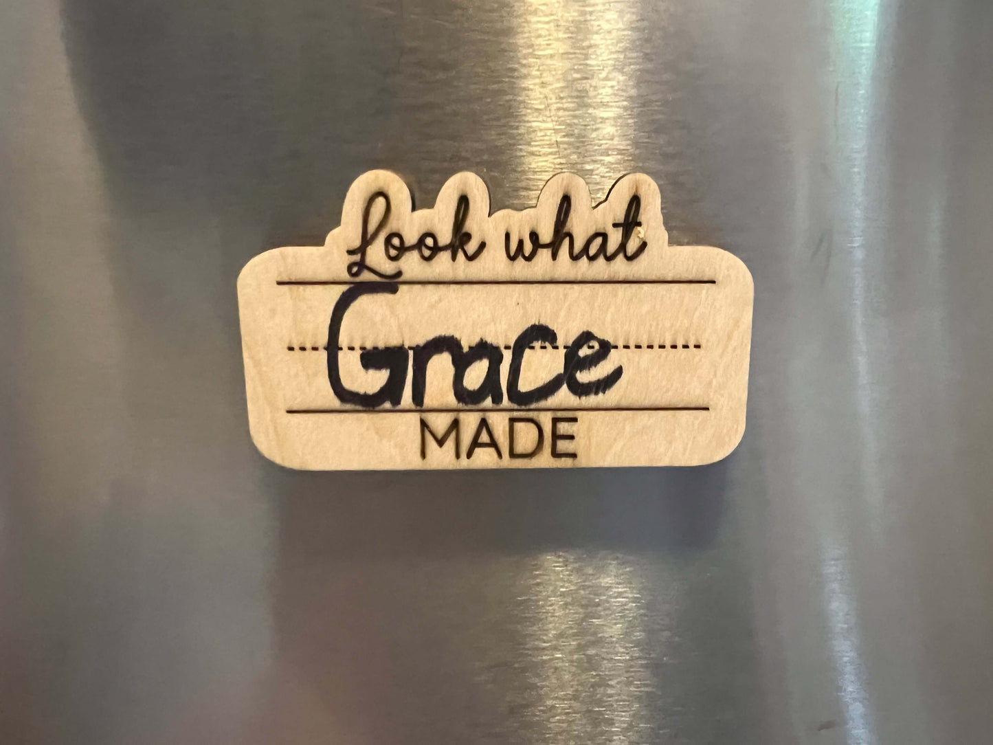 The Wet Nose Woodworks Look What I Made Fridge Magnet lets you proudly display and personalize your childs art or schoolwork with their name in colorful marker, adding a natural wood touch to your fridge.