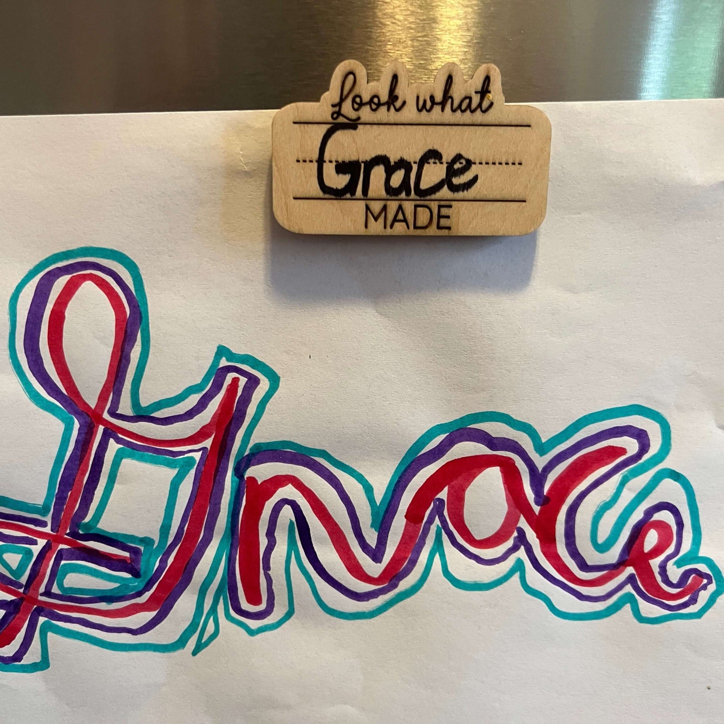 The Wet Nose Woodworks Look What I Made Fridge Magnet lets you proudly display and personalize your childs art or schoolwork with their name in colorful marker, adding a natural wood touch to your fridge.