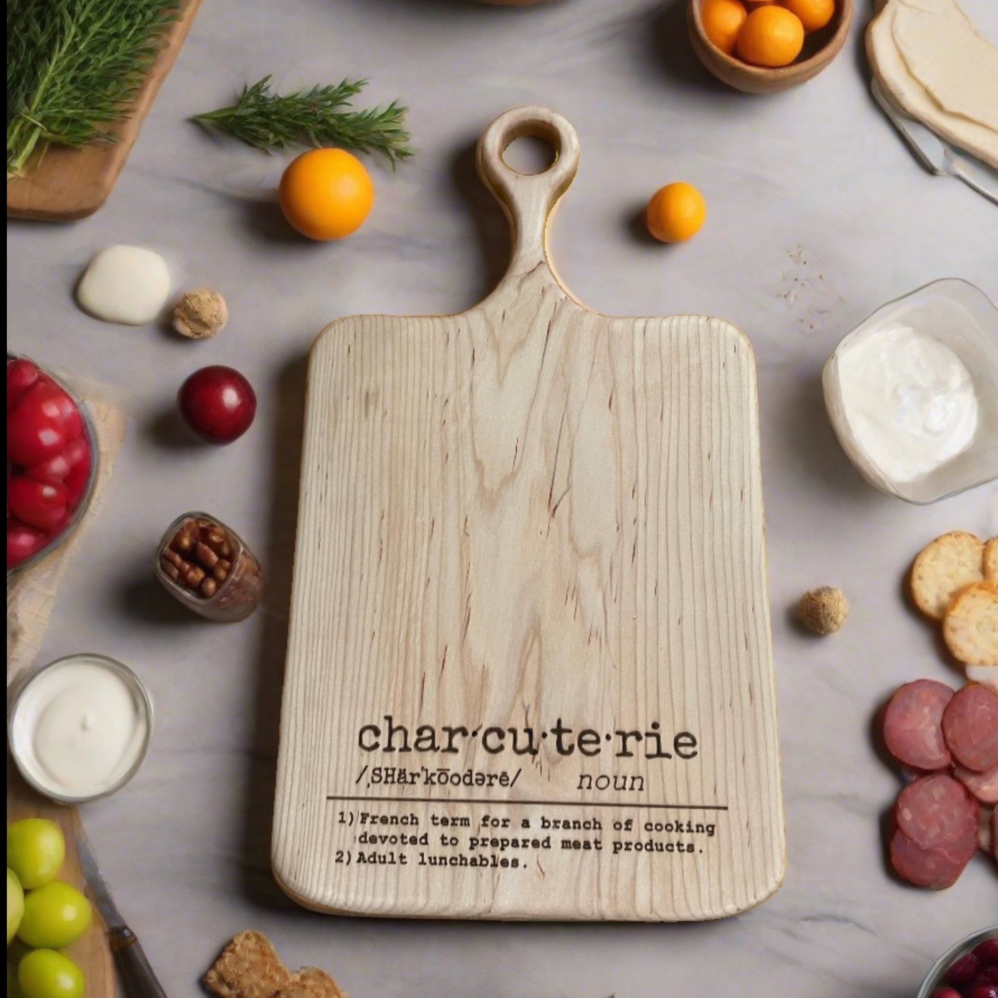 The Wet Nose Woodworks Maple Charcuterie Board with definition engraving rests on marble, topped with meats, cheese, crackers, herbs, nuts, fruit, and dip—ideal for your next “adult lunchable.”.